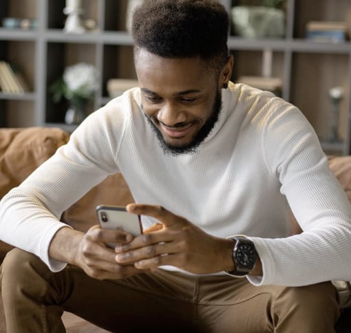 a man sitting on a couch smiling at his smartphone