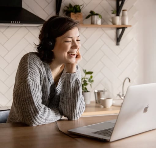 young woman with headphones laughing in front of her computer.